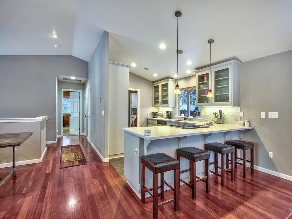 Kitchen with white quartz island, dark wooden stools, glass-front cabinets, and stainless steel appliances.