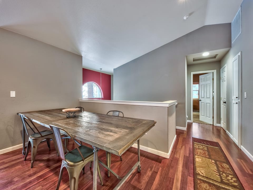 Dining area with a reclaimed wood table, metal chairs on hardwood floors, and an arched window with red accent wall.