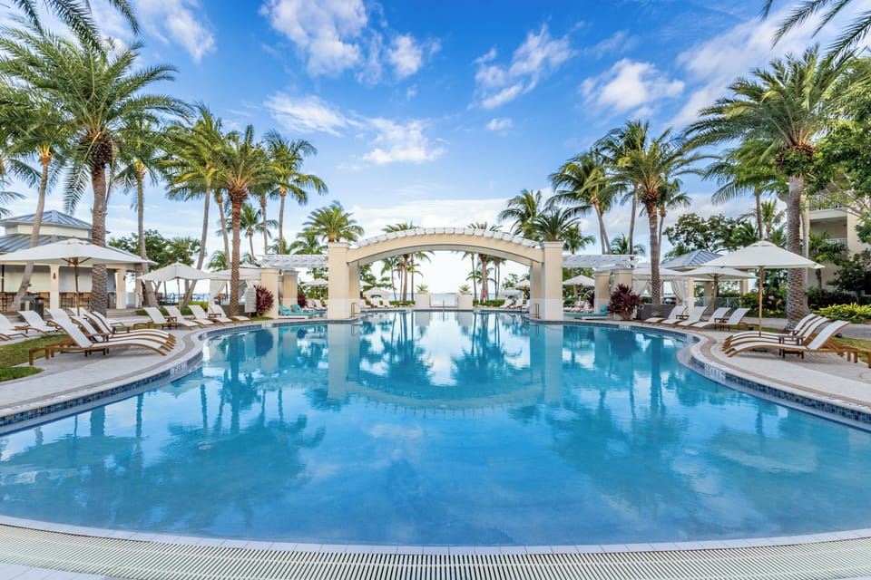 Tropical resort-style pool with bridge, palm trees, and ocean views.