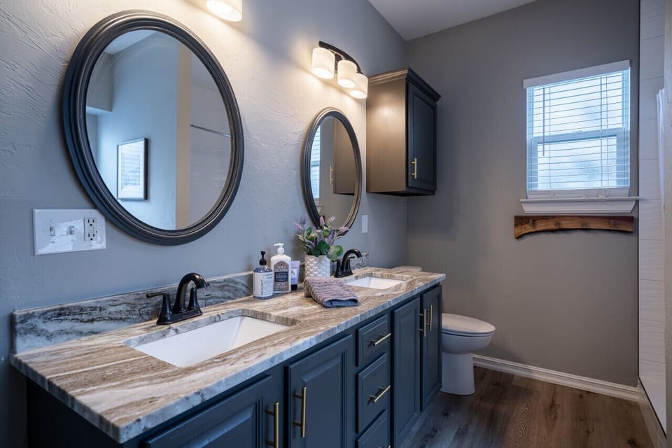 Bathroom with a double vanity, cabinets and stone counters, with two round mirrors and soap at each sink, ready for an easy morning routine