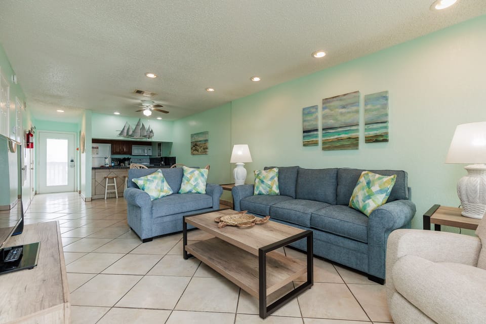 Relax in your coastal living space with ocean-themed decor, comfortable blue sofas, and an open kitchen perfect for beachside getaways.