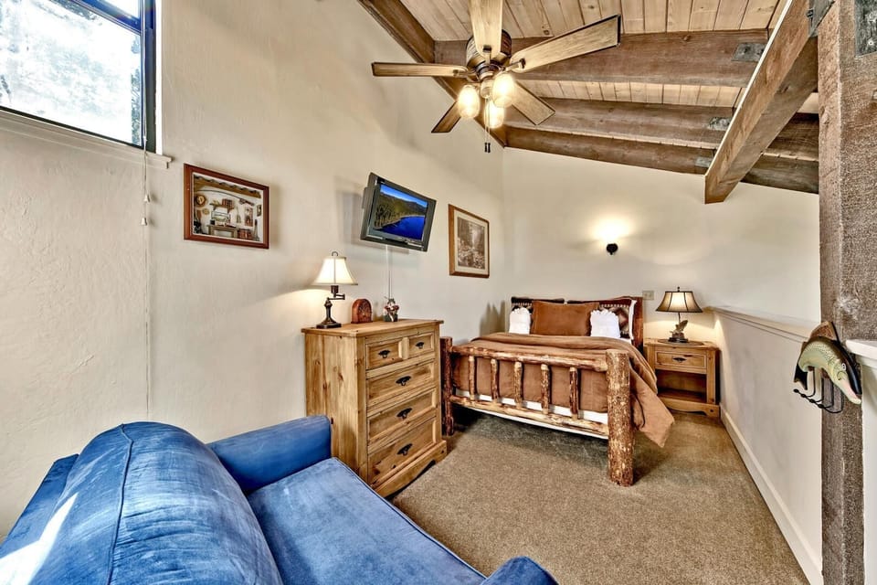 Relax in your rustic bedroom with exposed wooden beams, cozy log bed, and blue seating area perfectly positioned near the window.