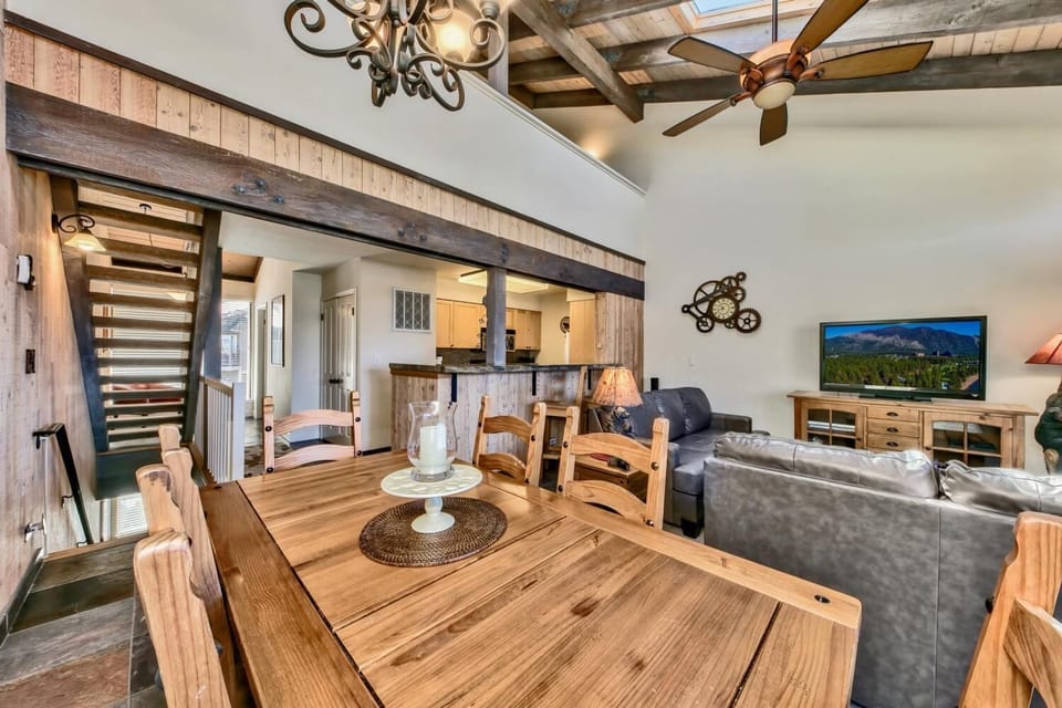 Relax in your rustic-chic living space with exposed beams, warm wood dining table, and cozy leather seating beneath elegant chandeliers.