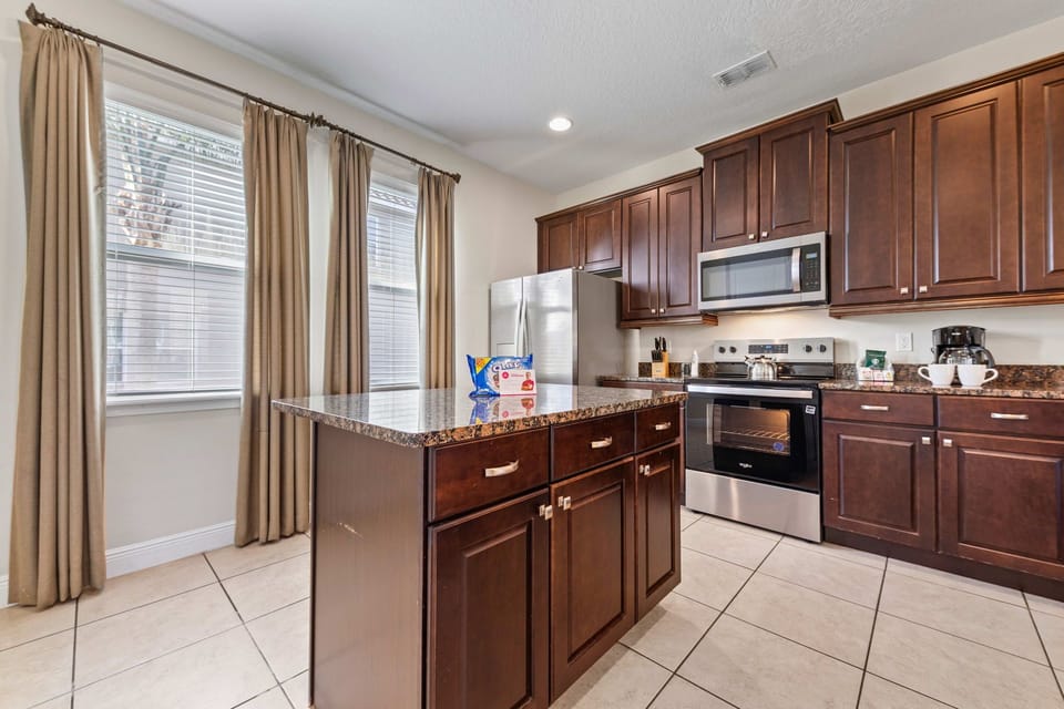 Sleek kitchen of the Home in Kissimmee Florida - Integrated appliances for a seamless and stylish appearance - High Chairs and breakfast bar - Coordinated kitchen decor for a polished and inviting atmosphere