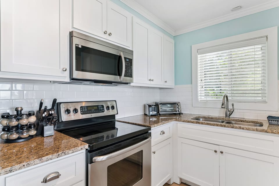 Your fully equipped kitchen features modern stainless appliances, granite counters, and crisp white cabinetry—perfect for preparing meals while natural light streams through the window.
