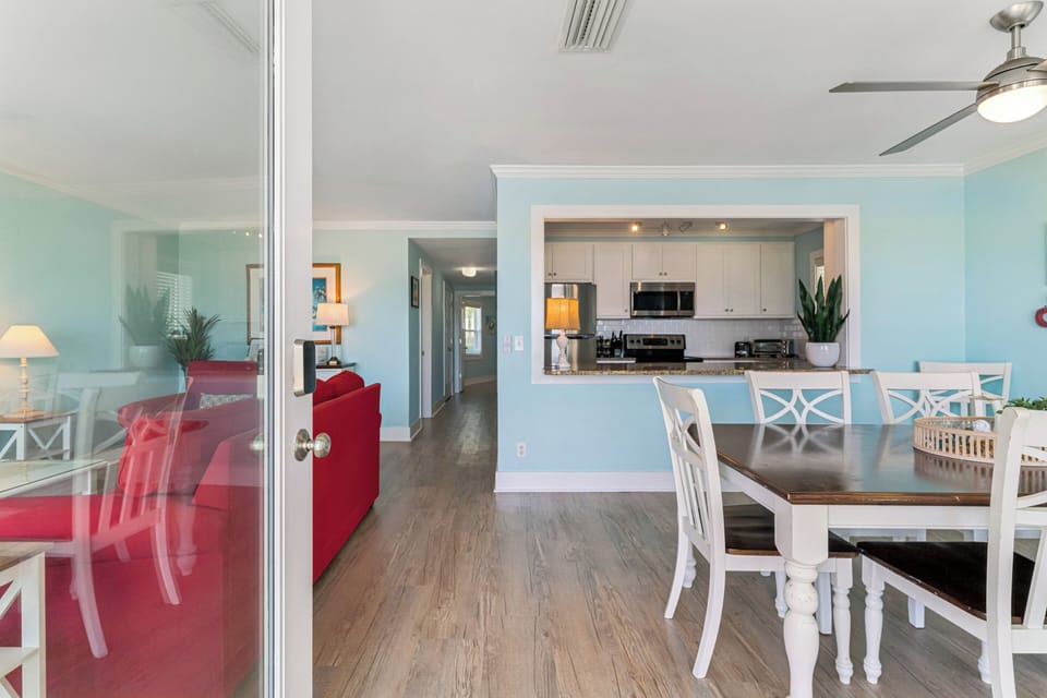 Step into your open coastal retreat where calming blue tones, wood floors, and modern kitchen comforts blend seamlessly with beach-house charm and inviting dining space.