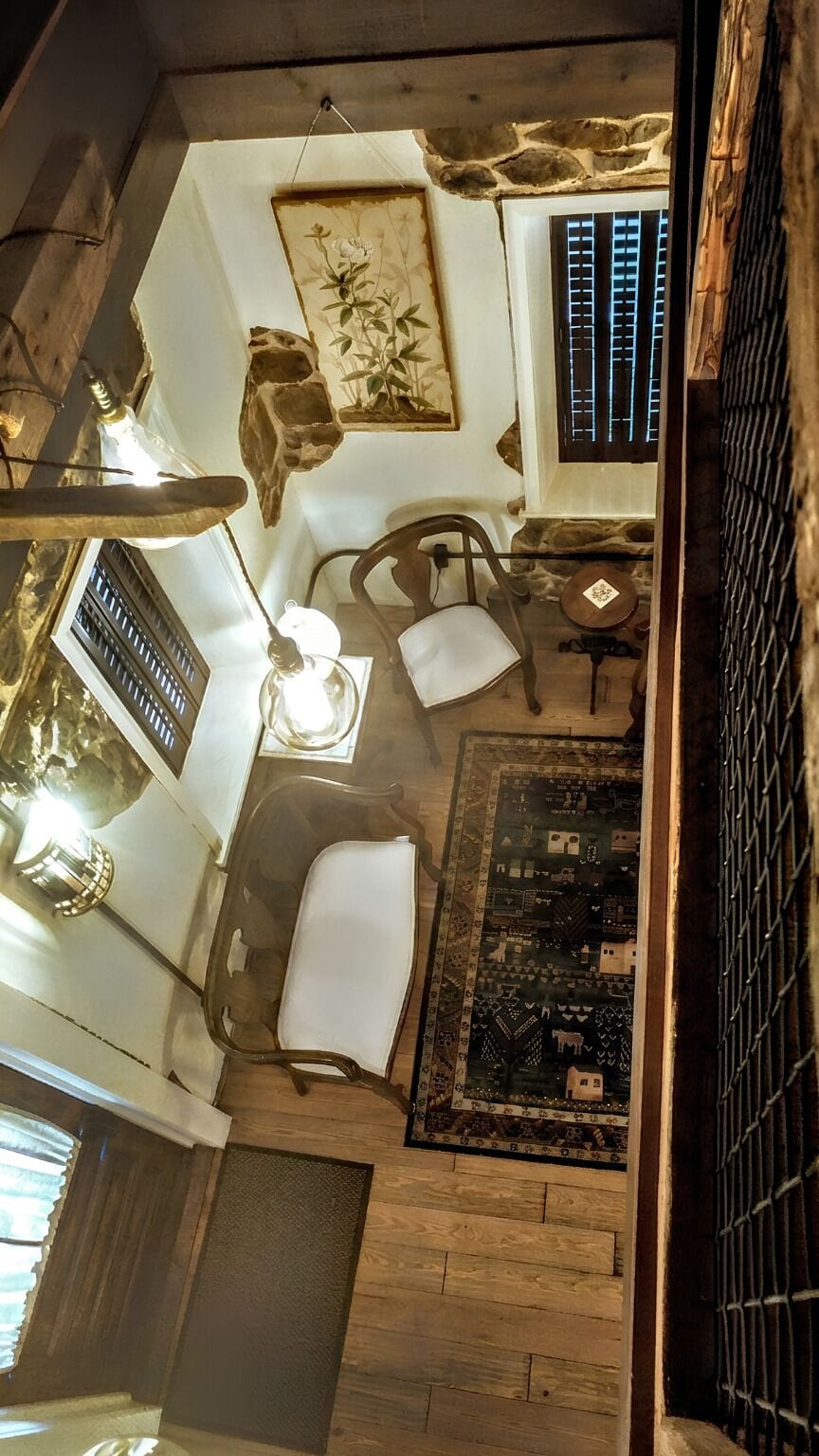 Upper Level Bedroom seating area opens to the living area on the historic house main level just past railing. Chairs have been replaced with a custom L-shaped sofa