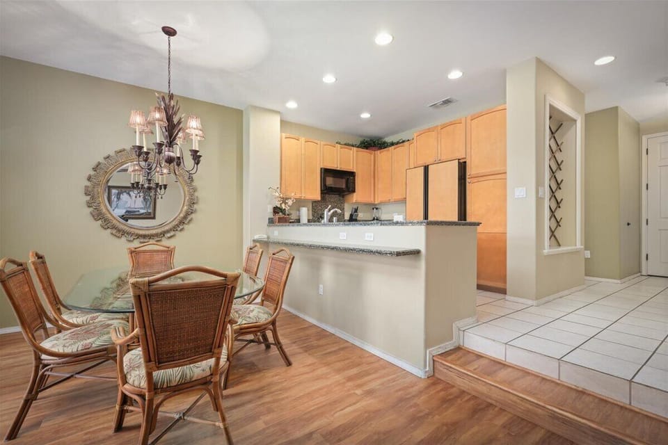 Your open-concept dining and kitchen space features warm wood floors, an elegant chandelier, and fully equipped kitchen with modern appliances. The breakfast bar offers casual seating for meals.