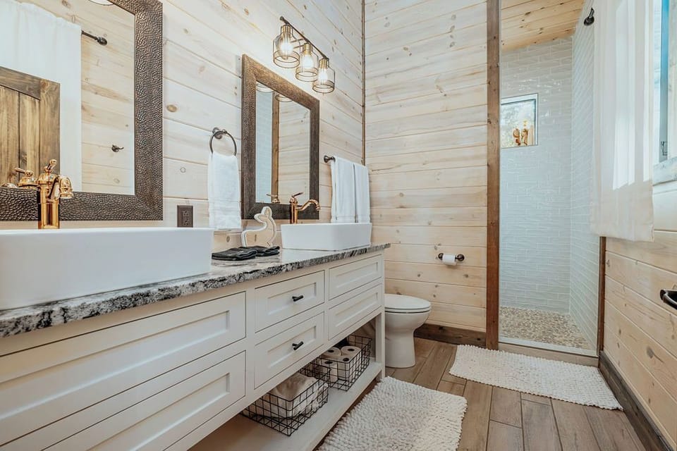 A beautifully designed bathroom with dual vanity sinks, a walk-in shower, and a mix of natural wood and white finishes, combining luxury with a rustic touch.