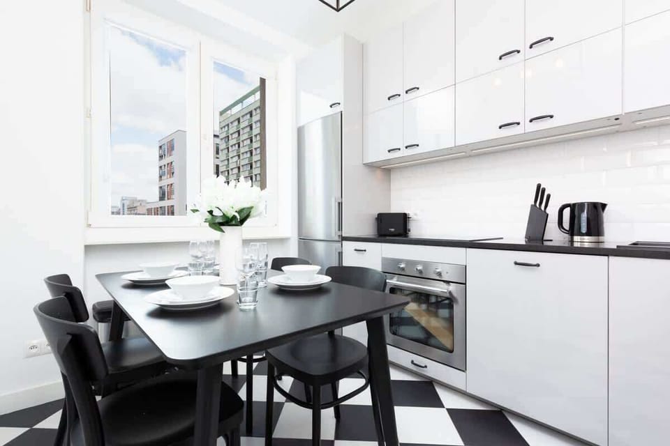 Kitchen with dining area which is formed by a disagner black table with wrap-around chairs. The kitchen shows an oven, toaster, knife set and electric kettle. 