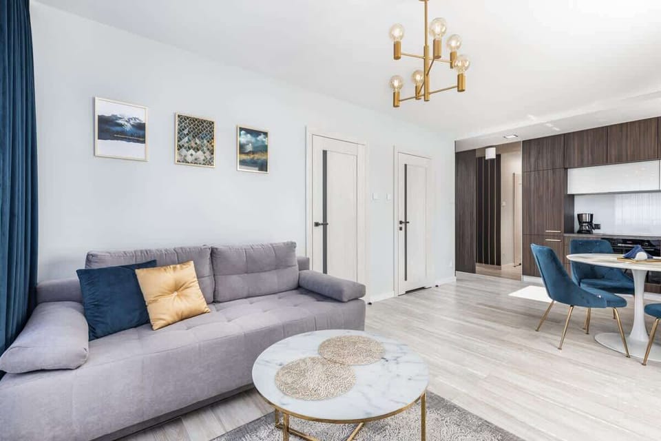 Living room with a gray sofa and a round coffee table. The decor features subtle, modern touches and a chandelier.
