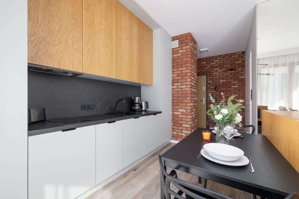 A modern kitchen with black countertops, wooden cabinets, and a minimalist dining area.
