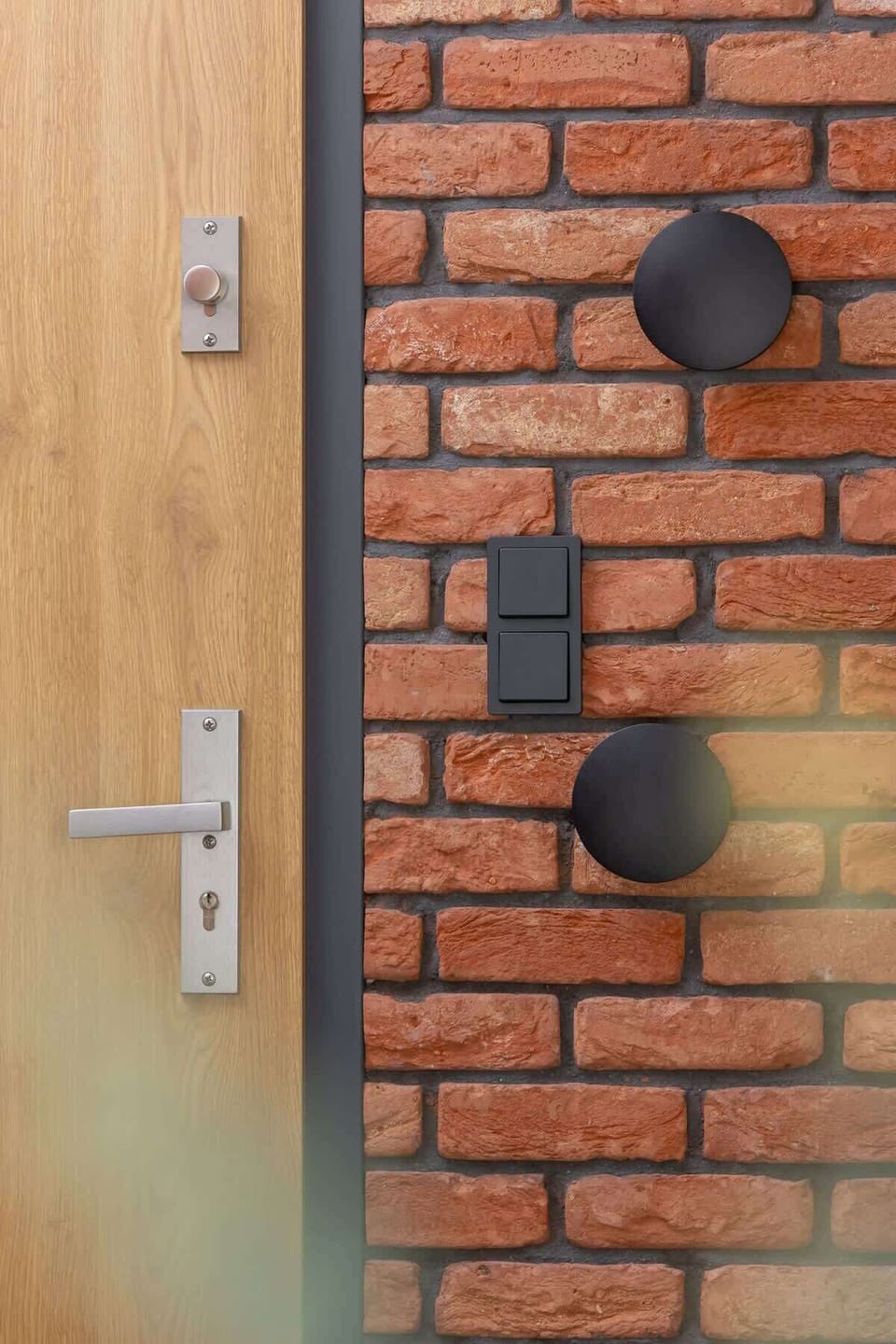 A close-up of a wooden door with a brick wall, featuring modern black light switches.
