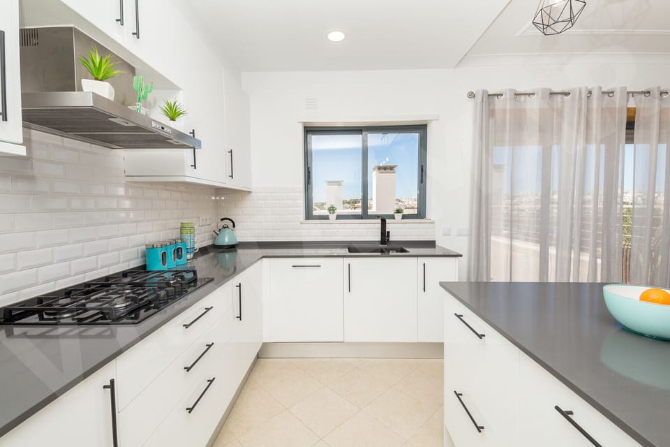 Kitchen cooking area in Apartment Vista Mar, Lagos, featuring a gas hob, stainless steel extractor hood, and bright natural light from the window with views, perfectly designed for holiday cooking in the Algarve