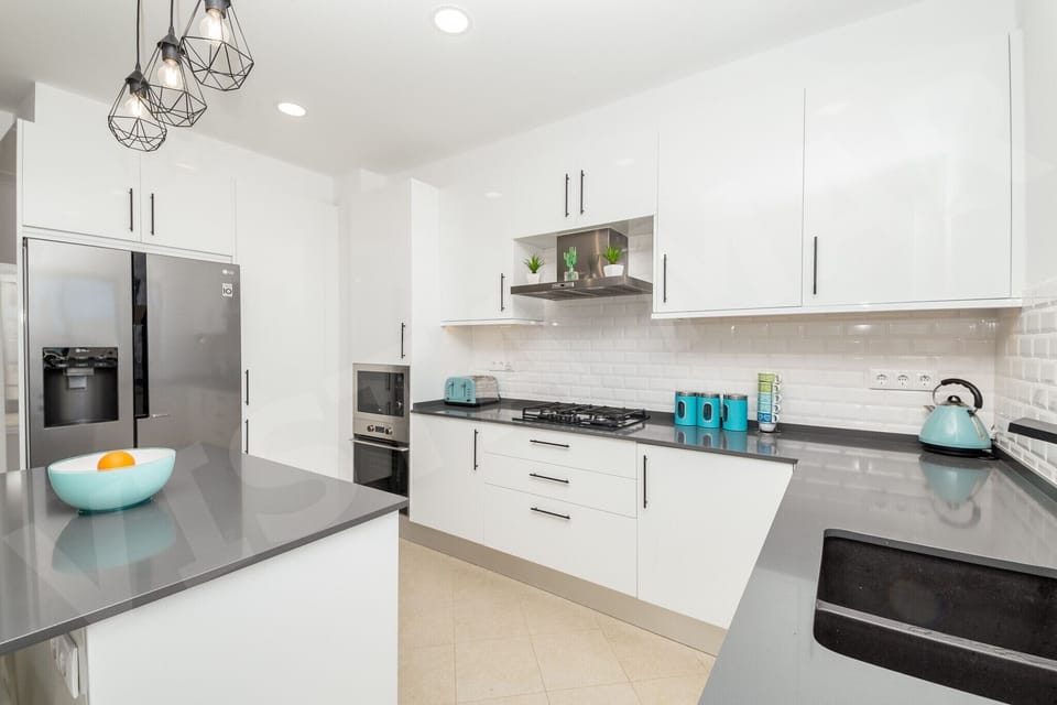 Well-equipped kitchen in Apartment Vista Mar, Lagos, showcasing a large fridge-freezer, built-in oven, and ample storage space with modern white cabinetry and pendant lighting, everything you need for self-catering in the Algarve