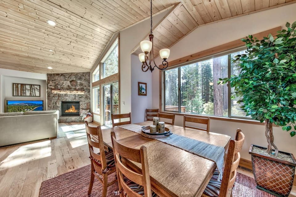 Gather around the rustic wooden table beneath soaring wood-beam ceilings, where forest views frame your meals and the stone fireplace awaits cozy evenings.
