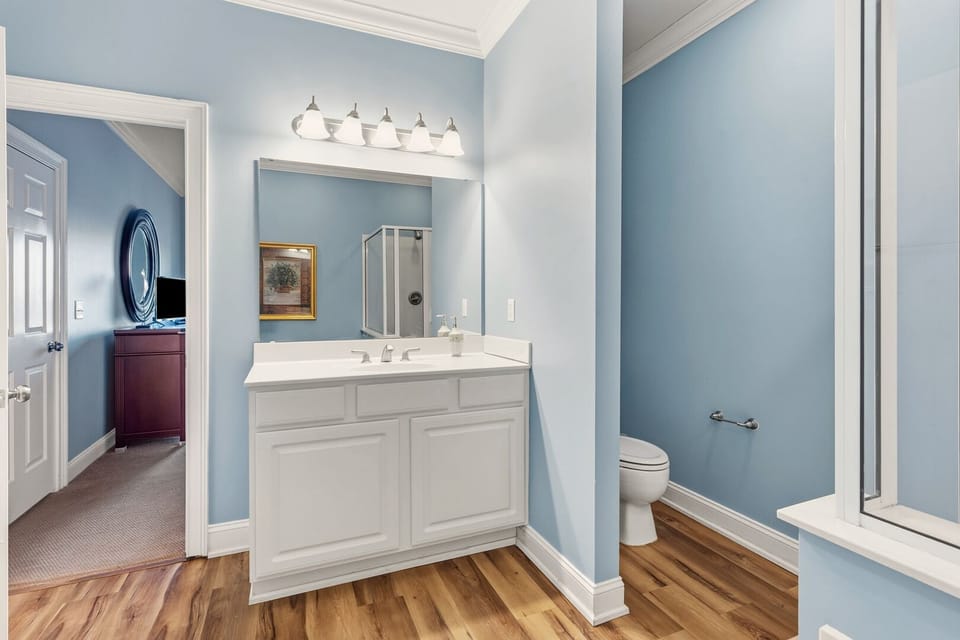 White vanity and a lit mirror against blue walls at Point Marsh 2418 in Cherry Grove, North Myrtle Beach