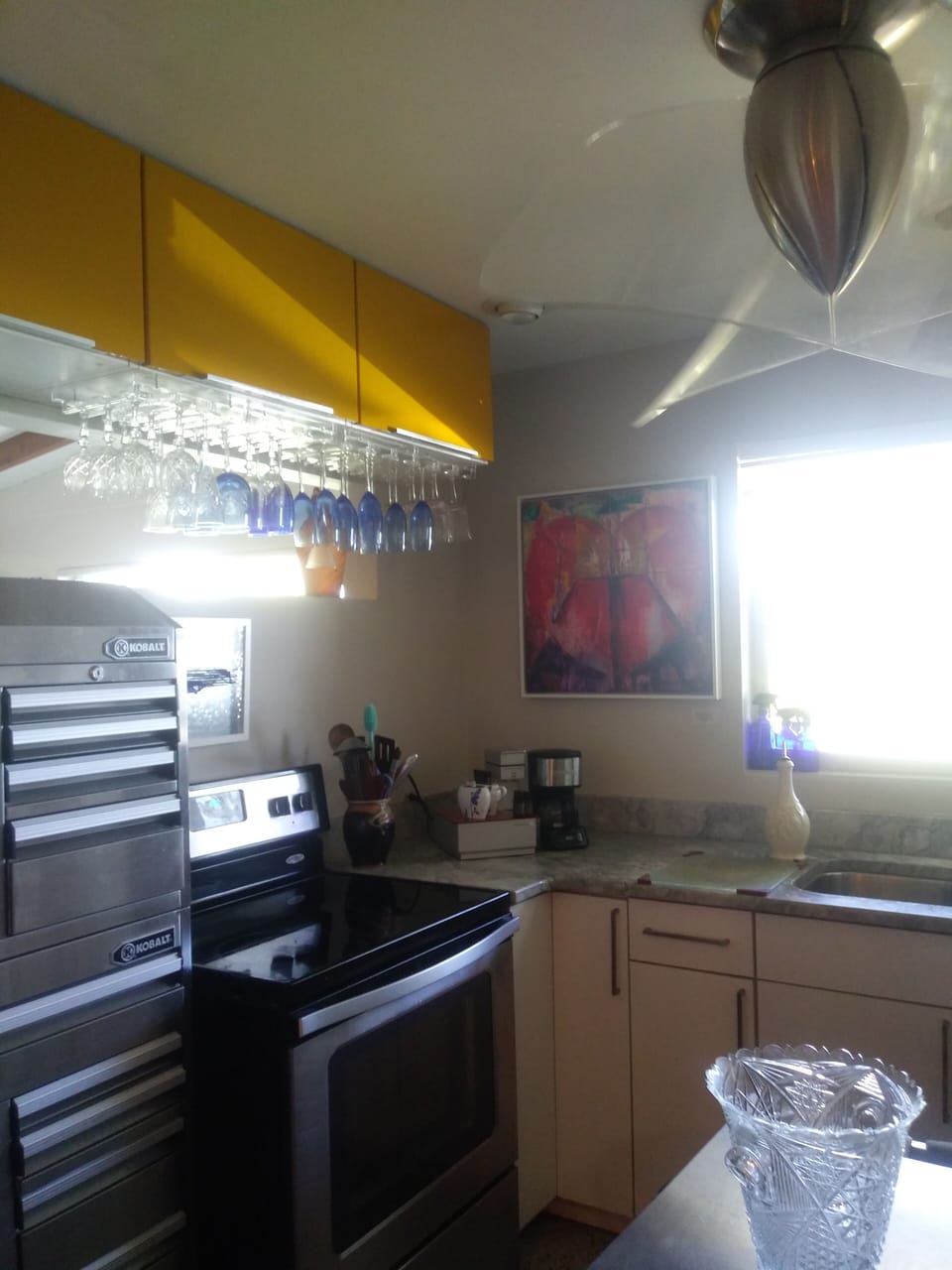 Left side of kitchen with upper cabinets, storage tool box, stove & double sink.