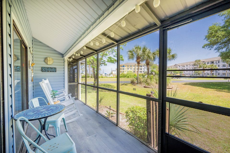 The screened porch features a cozy seating area with a decorative table, perfect for enjoying views of lush greenery