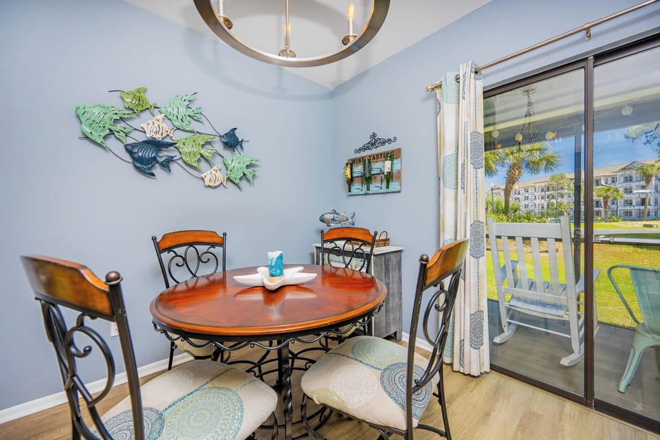 The dining area features a round wooden table, stylish chairs, and a view of the outdoor seating area surrounded by greenery