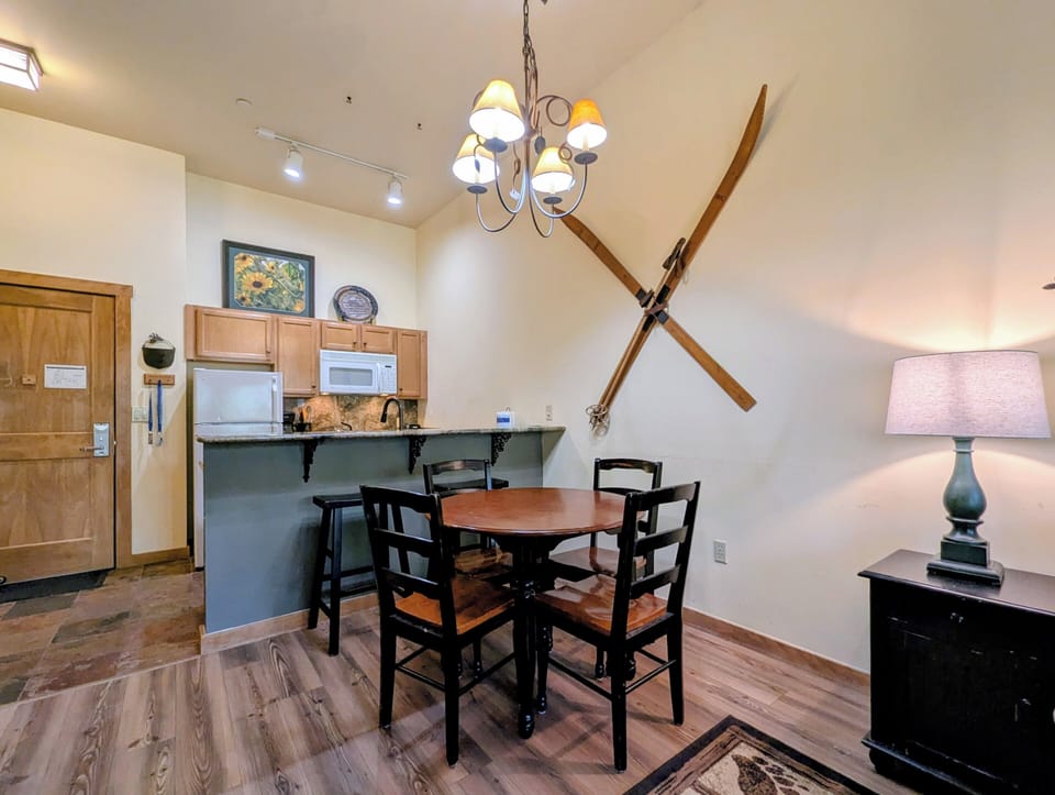 Your cozy dining space invites shared meals beneath vaulted ceilings, where charming ski décor adds mountain character. The full kitchen awaits your culinary adventures, with granite counters and modern appliances ready for your use.