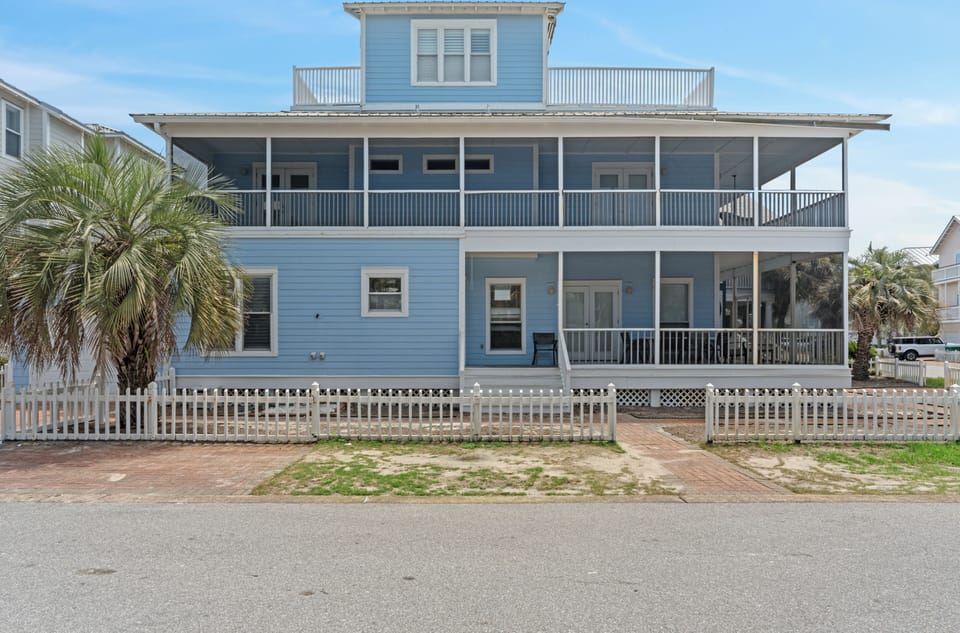 Coastal exterior with multiple covered porches, palm trees, and an easy beach-town feel.