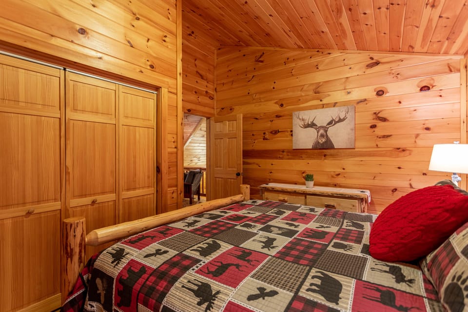 Cozy mountain nights await in this log-framed bedroom at Bearadise At Blue Ridge, dressed in classic wildlife quilts and rustic pine.