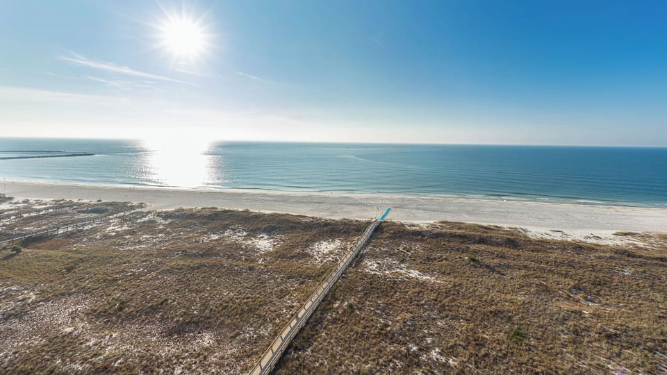 Glowing sand meets the tranquil gulf waters under a bright sun, creating a serene beach atmosphere perfect for relaxation