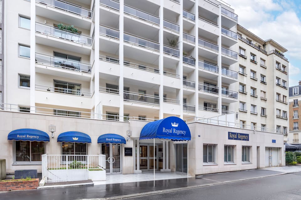 The elegant façade of Royal Regency Hotel, with its stylish exterior with balconies and signature blue canopies welcoming you to a luxurious stay.