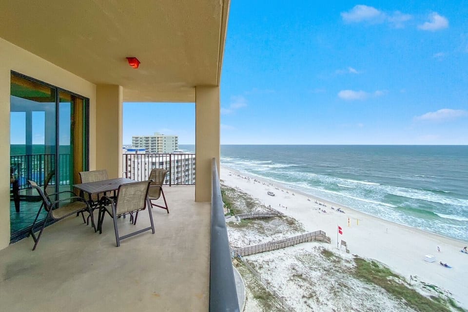 The balcony features a dining set with chairs, offering a direct view of the beach and gentle waves lapping the shore