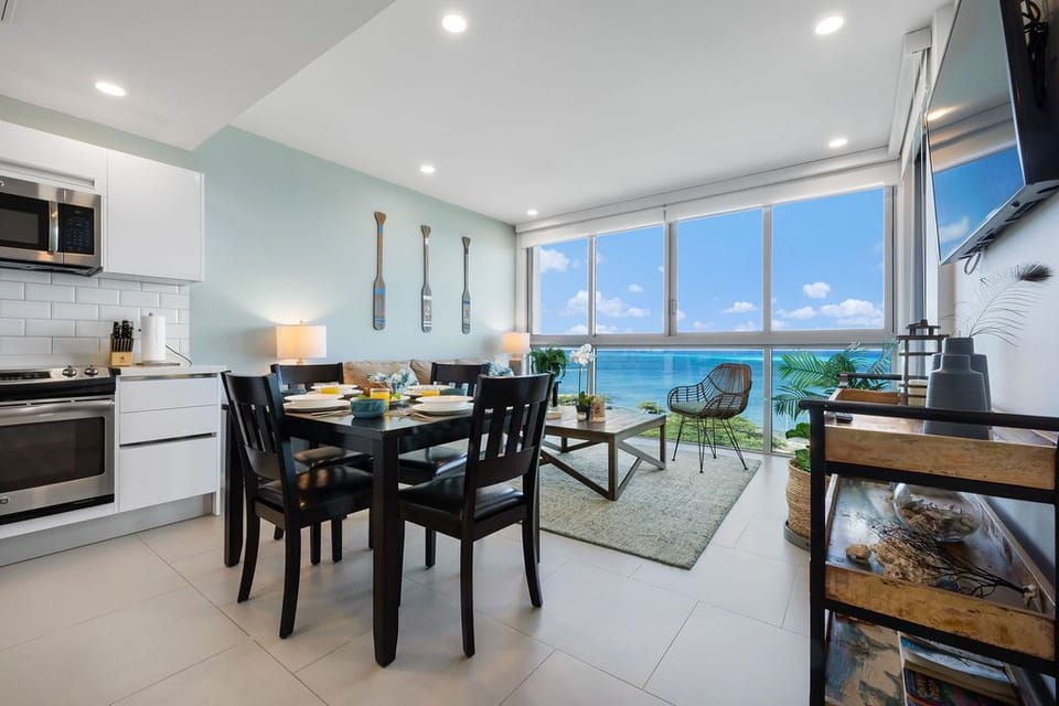 Imagine sipping morning coffee at your dining table while gazing at turquoise waters—the open kitchen, bright coastal décor, and floor-to-ceiling windows invite you to soak in every moment.