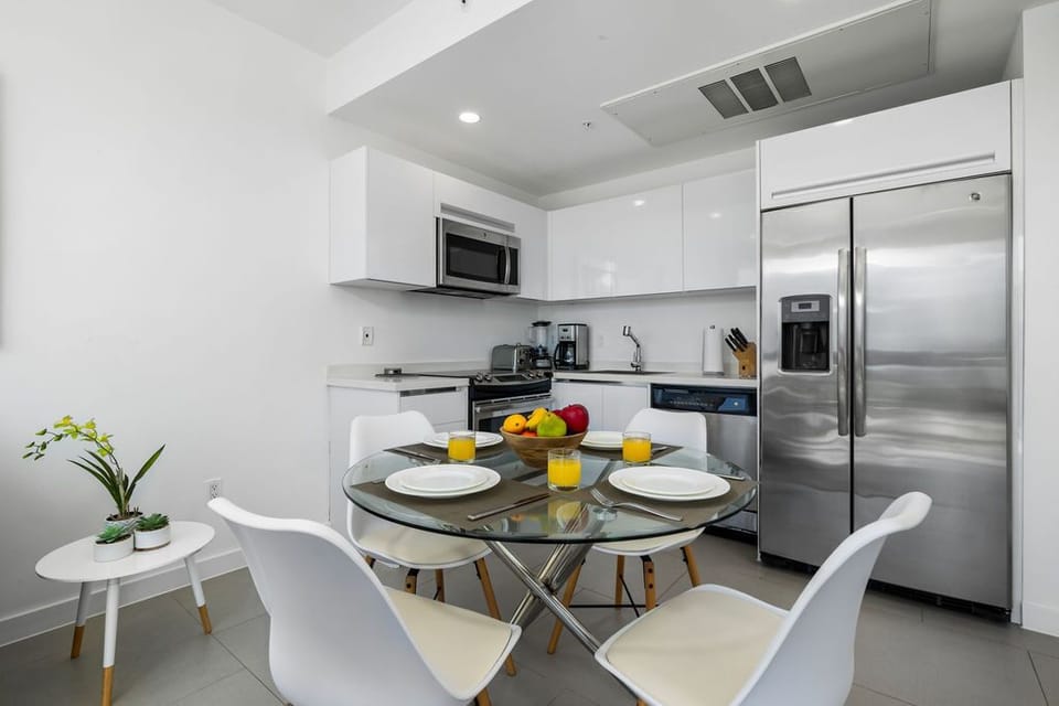 Your sleek, modern kitchen awaits with stainless-steel appliances, a spacious fridge, and a cozy glass dining table—perfect for savoring morning coffee and home-cooked meals together.