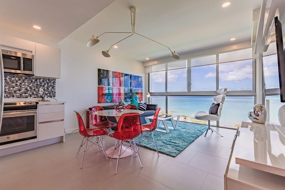 Bright open-plan living with vibrant artwork and stunning oceanfront views. The modern kitchen flows into a cozy seating area—perfect for your morning coffee ritual overlooking endless blue horizons.