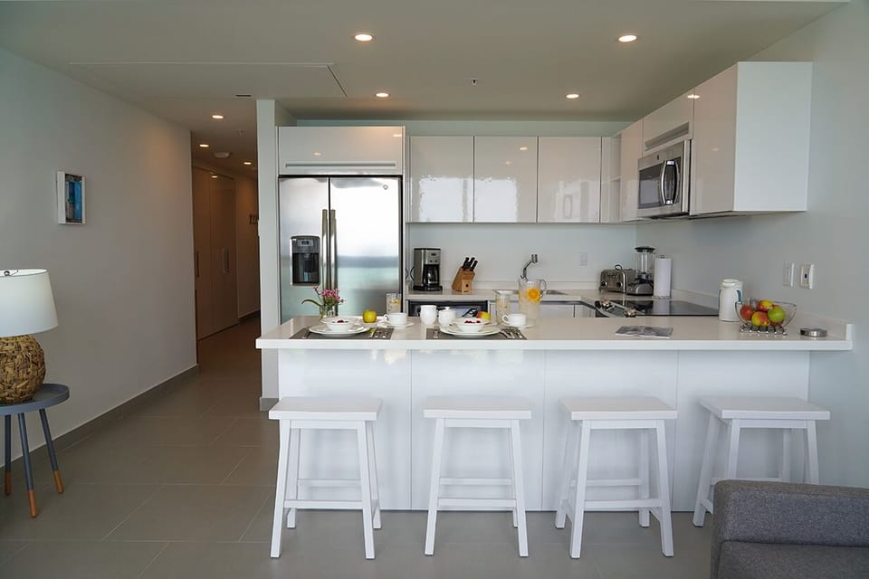 Your bright, modern kitchen features sleek white cabinetry, stainless steel appliances, and a spacious island with bar seating—perfect for casual meals or morning coffee together.