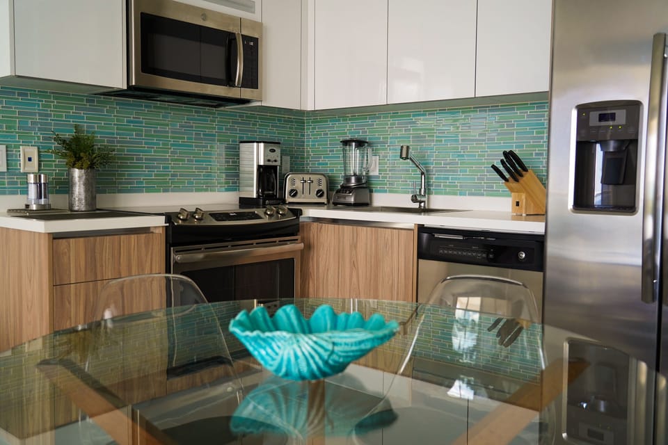 Modern kitchen with stunning turquoise tile backsplash, stainless steel appliances, and sleek counters—your perfect space to whip up meals while savoring coastal-inspired design and all the comforts of home.