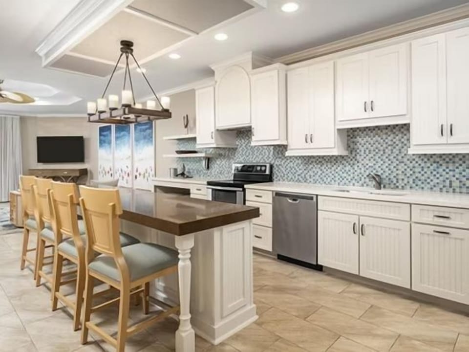 White kitchen with mosaic tile backsplash, large island, and full stainless steel appliance suite