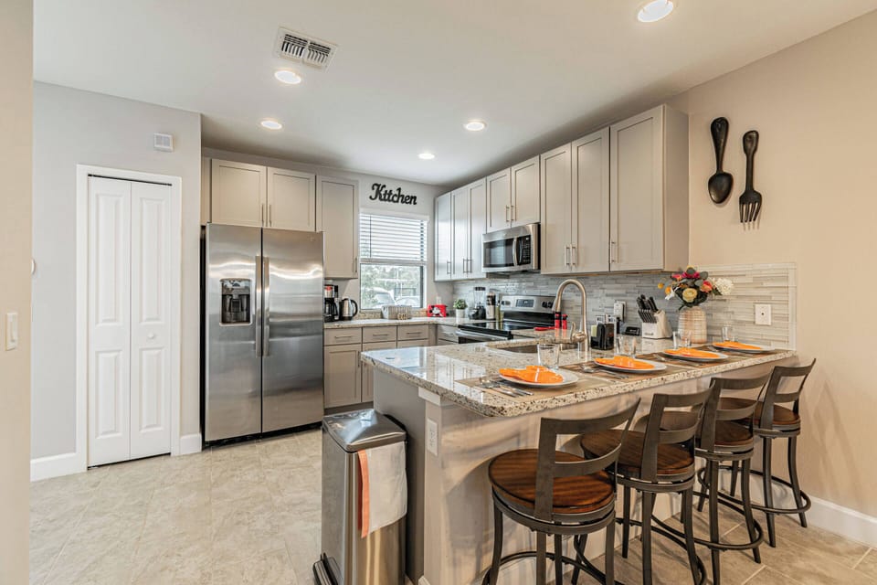This bright kitchen boasts sleek gray cabinetry and stainless steel appliances, inviting culinary adventures. The spacious island with stylish bar stools is perfect for casual dining or morning coffee, enhancing your experience.