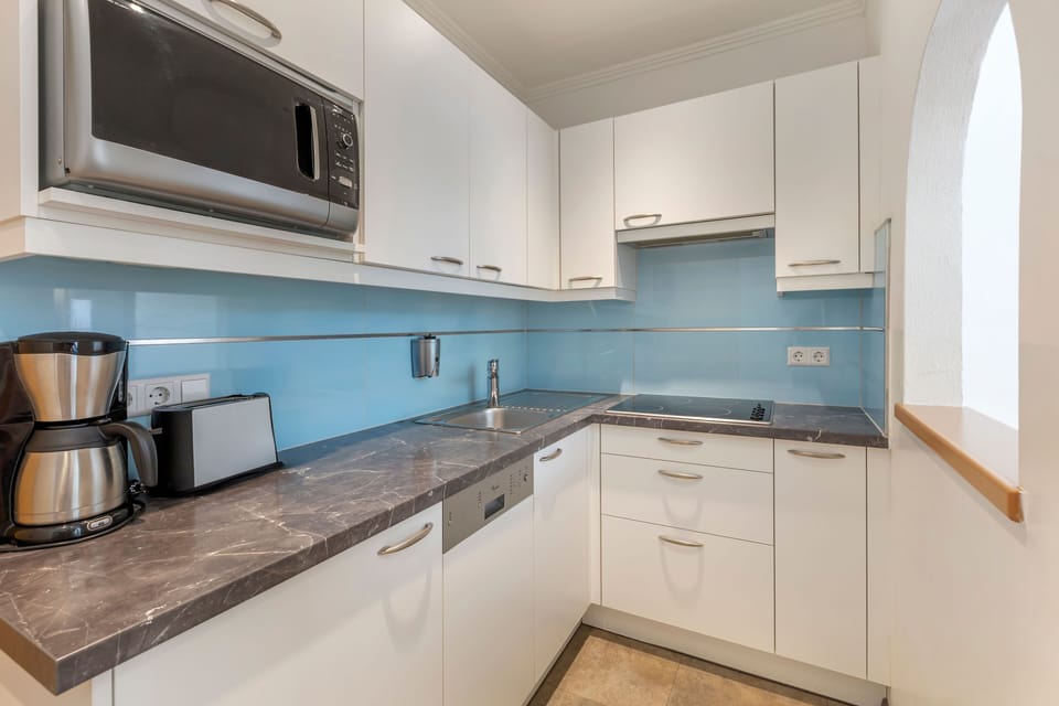 The kitchen showcases sleek, white cabinetry and a contemporary style, equipped with essential appliances such as a stove and coffee machine, making cooking a delight.