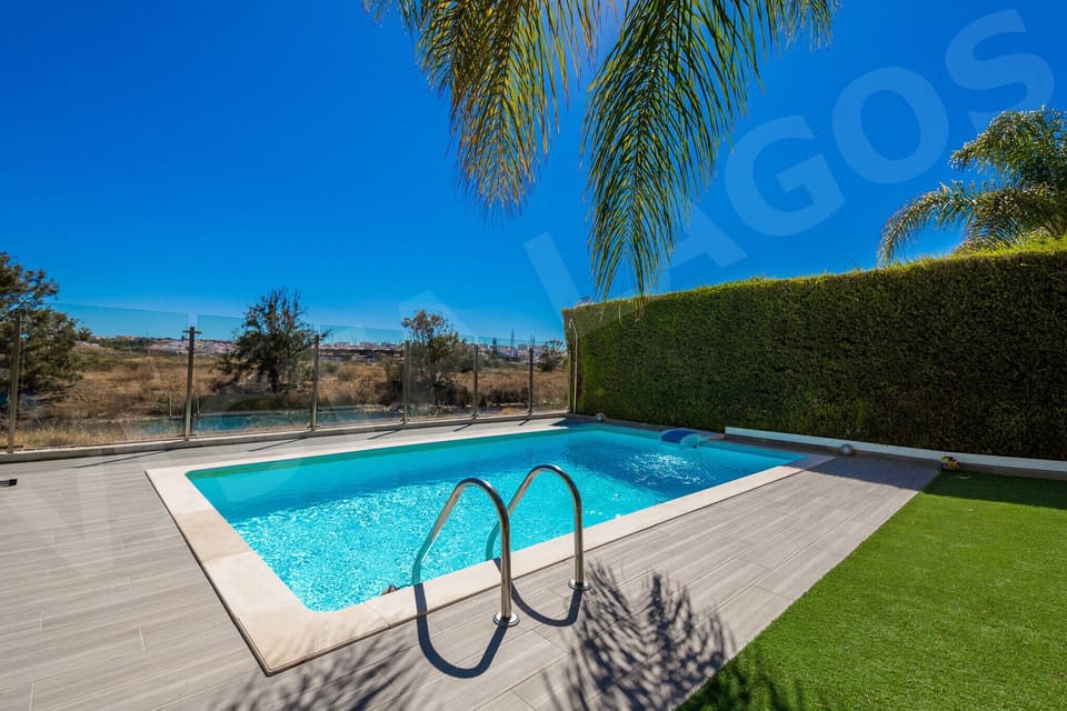 Private swimming pool with chrome ladder and wooden deck surround at Casa Vista Lago, a 4-bedroom holiday townhouse in Lagos, Algarve, featuring lush garden landscaping and clear blue pool water