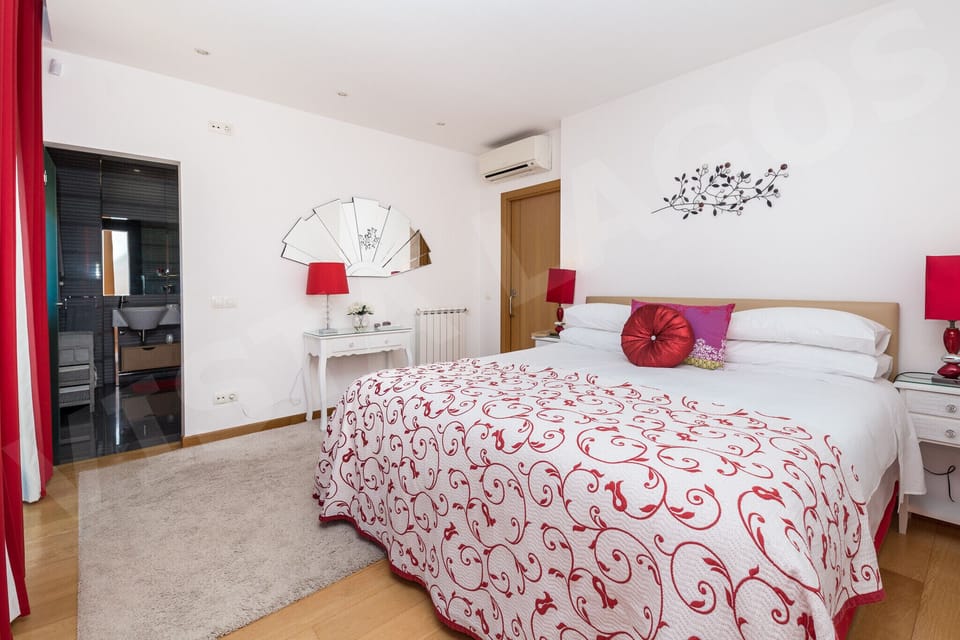 Bright double bedroom with red and white floral bedding at Casa Vista Lago, a holiday townhouse in Lagos, Algarve. Features decorative red cushions, matching table lamps, butterfly wall art and wooden flooring.