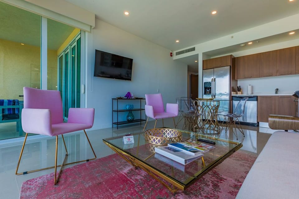 Stylish open living space featuring modern pink seating, gleaming gold accents, and a fully equipped kitchen—your perfect home base for comfort and relaxation.