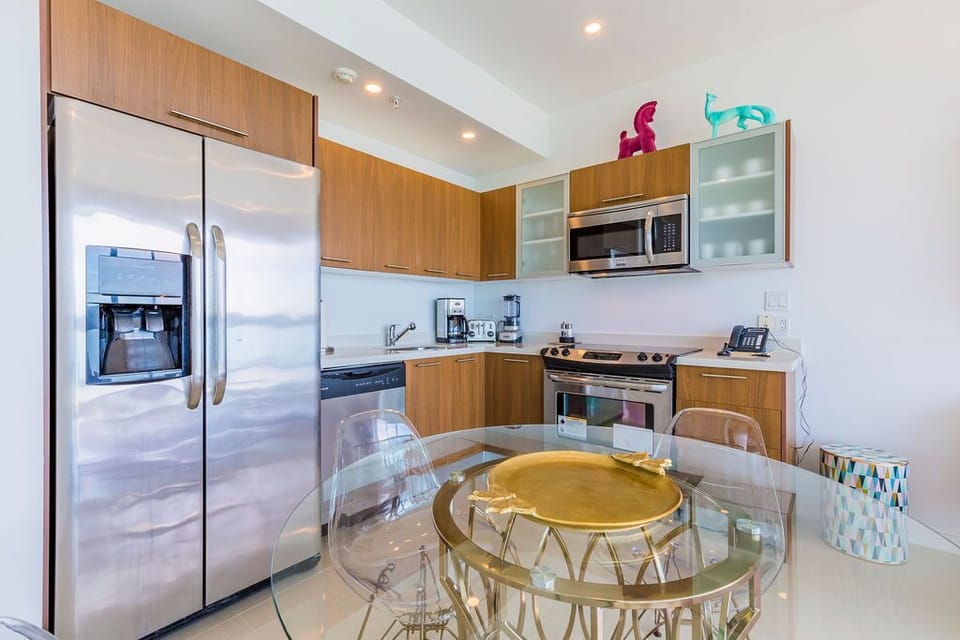 Your fully equipped kitchen features modern stainless appliances, sleek wood cabinetry, and a stylish glass dining table perfect for preparing and enjoying home-cooked meals during your stay.