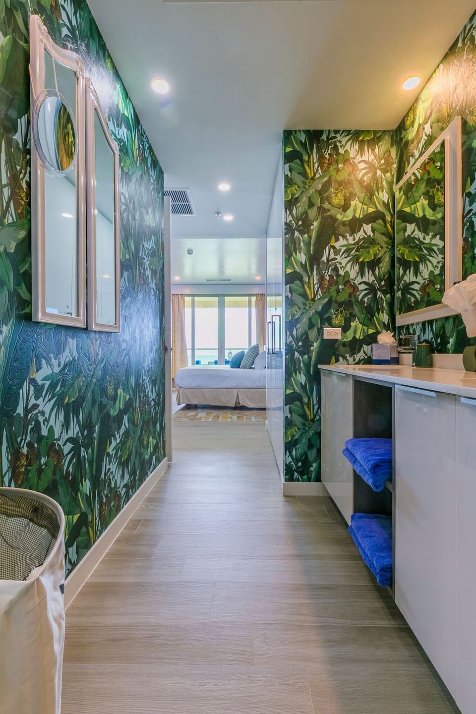 Step into a lush tropical retreat where vibrant botanical wallpaper and modern white cabinetry create your private sanctuary, leading to a peaceful bedroom beyond.