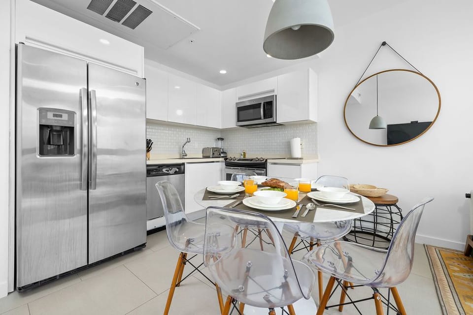 Your modern, well-appointed kitchen awaits with stainless appliances, bright white cabinets, and a stylish glass dining table where you can enjoy fresh orange juice and breakfast each morning.