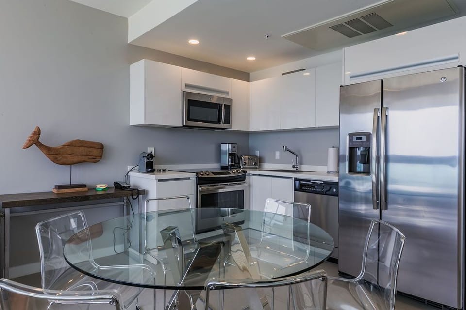 Your modern kitchen features sleek white cabinets, stainless steel appliances, and a glass dining table perfect for casual meals or morning coffee.