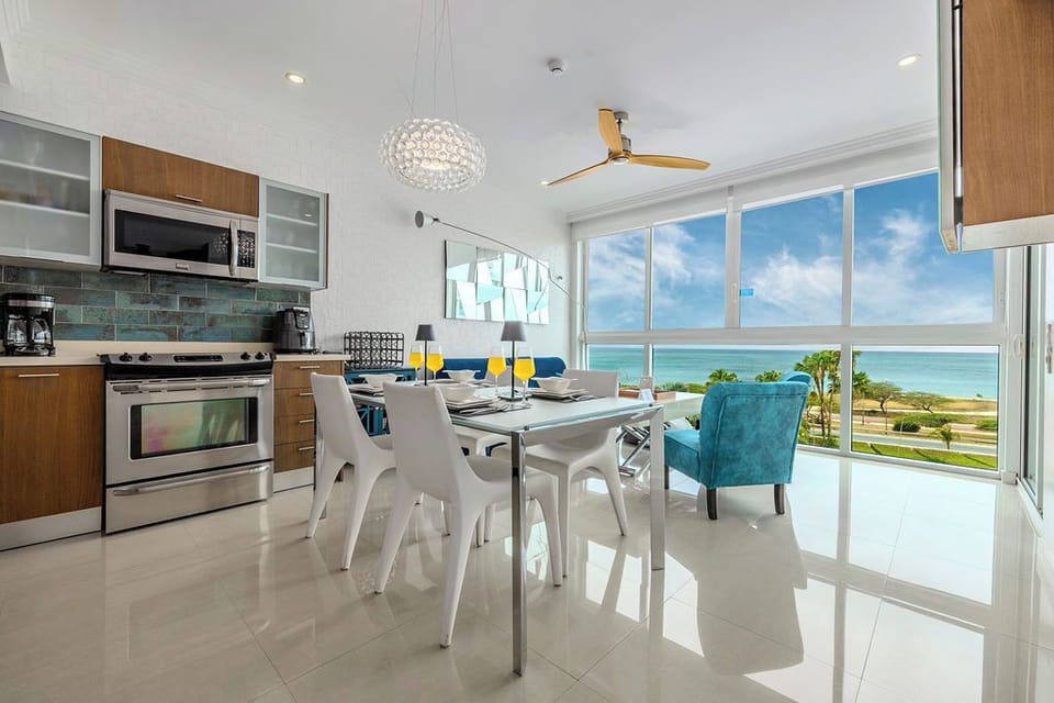 Your coastal retreat features a bright, open-plan kitchen and dining space with stunning turquoise water views stretching to the horizon through floor-to-ceiling windows.