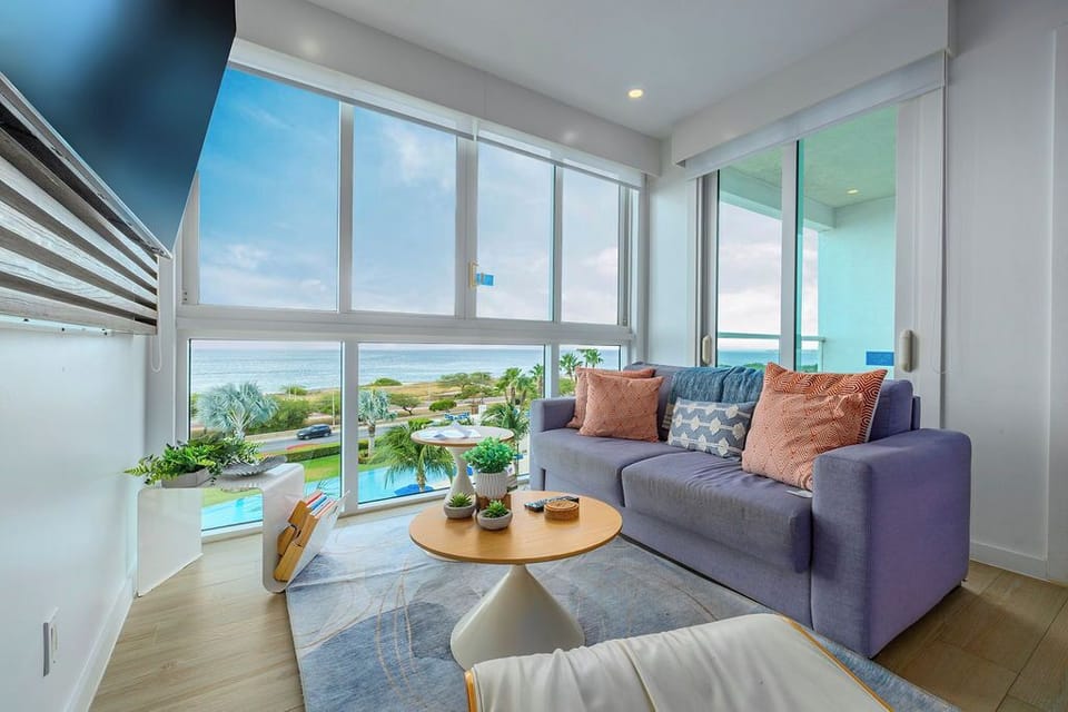 Sink into this bright living room where floor-to-ceiling windows frame stunning sea views. Your coastal retreat offers modern comfort with a cozy sofa, fresh tropical touches, and direct pool access just steps away.