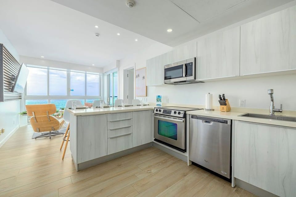 Your bright, fully-equipped kitchen flows seamlessly into the living area, framed by floor-to-ceiling windows revealing stunning ocean views just beyond.