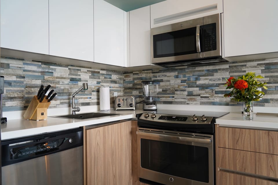 Modern kitchen equipped with stainless steel appliances, microwave, stove, and blender. White countertops and colorful backsplash create a bright, welcoming space for your meal prep.