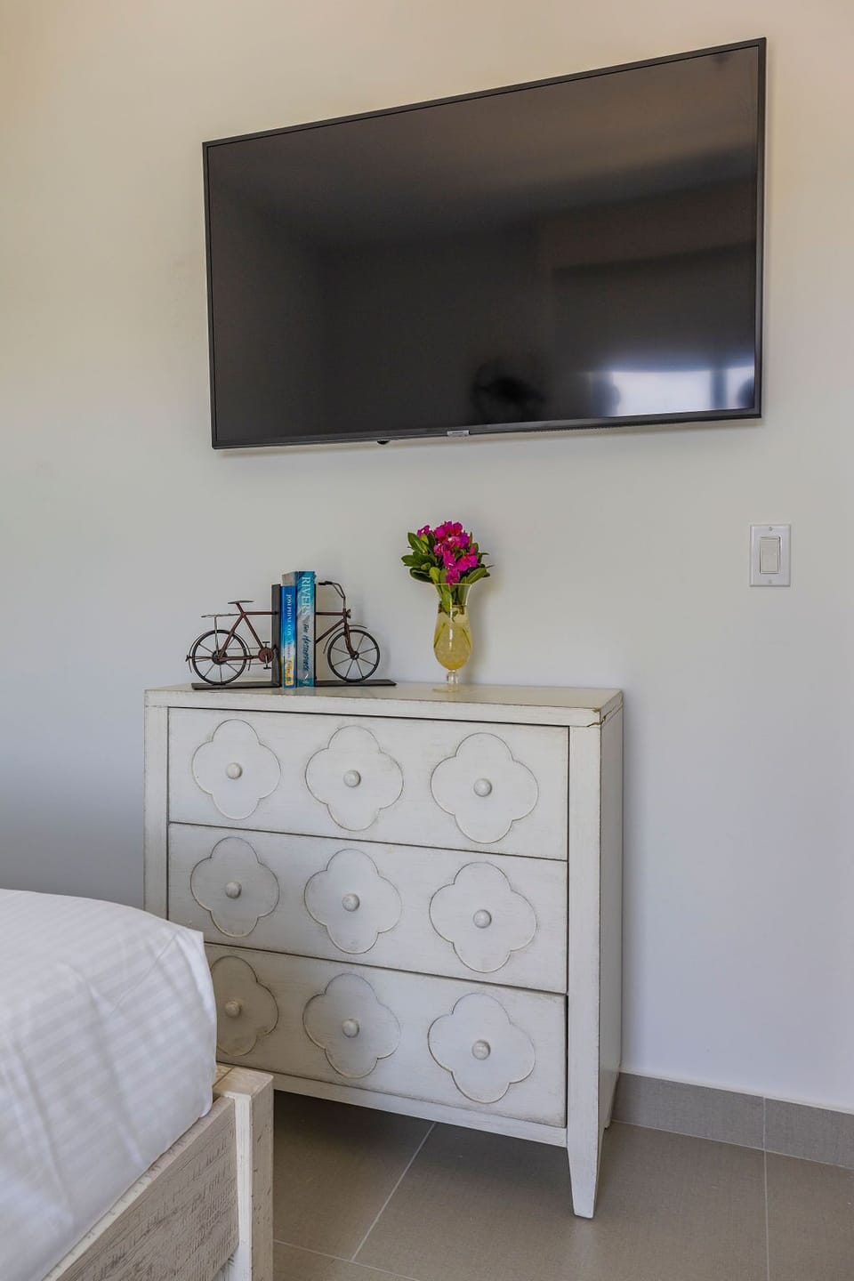 Your bedroom features a wall-mounted flat-screen TV and charming decorative dresser, with thoughtful touches like fresh flowers adding warmth to the space.